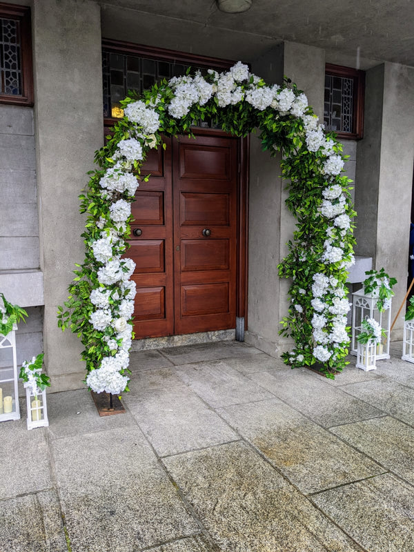 Extra large floral arch with lantern setss outside a church