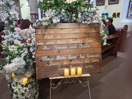 A rustic take a seat sign on an antique pedestal with florals 